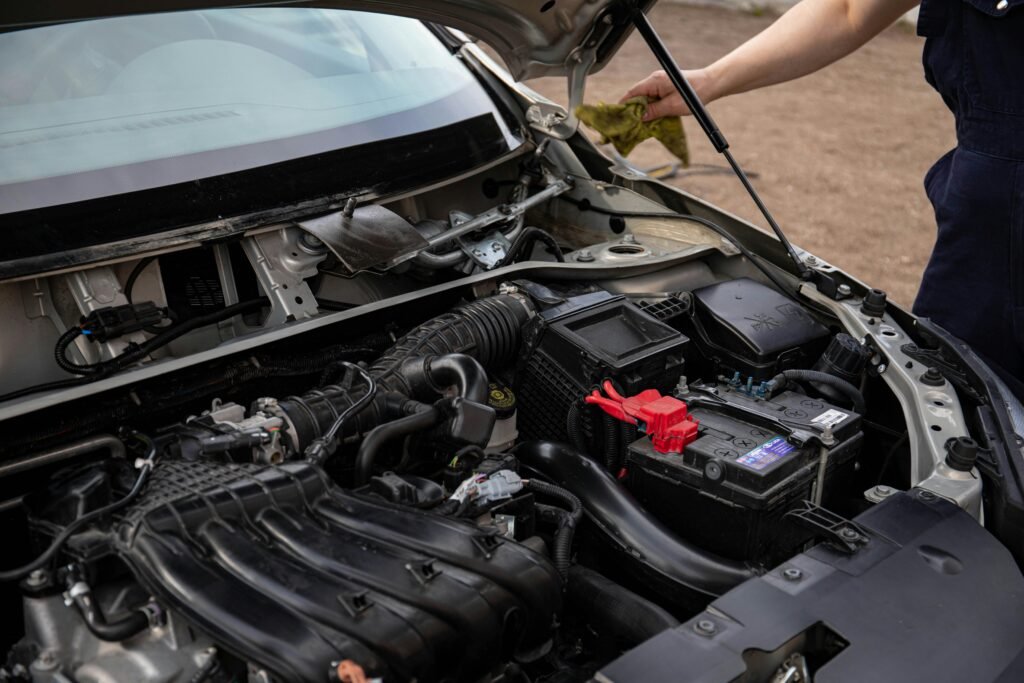 Mechanic inspecting car engine bay and battery during routine maintenance.